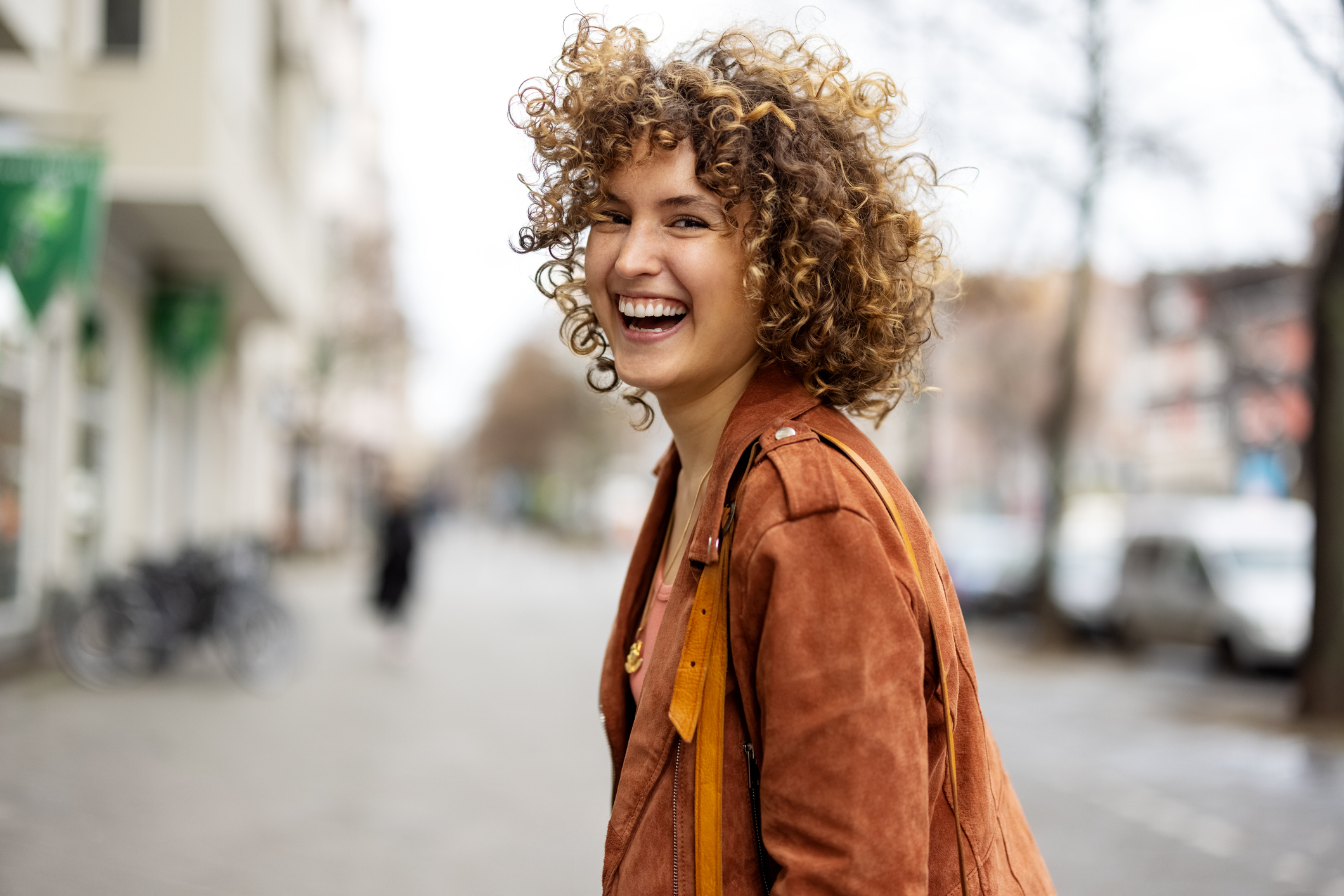 Smiling person with curly hair in a city street setting