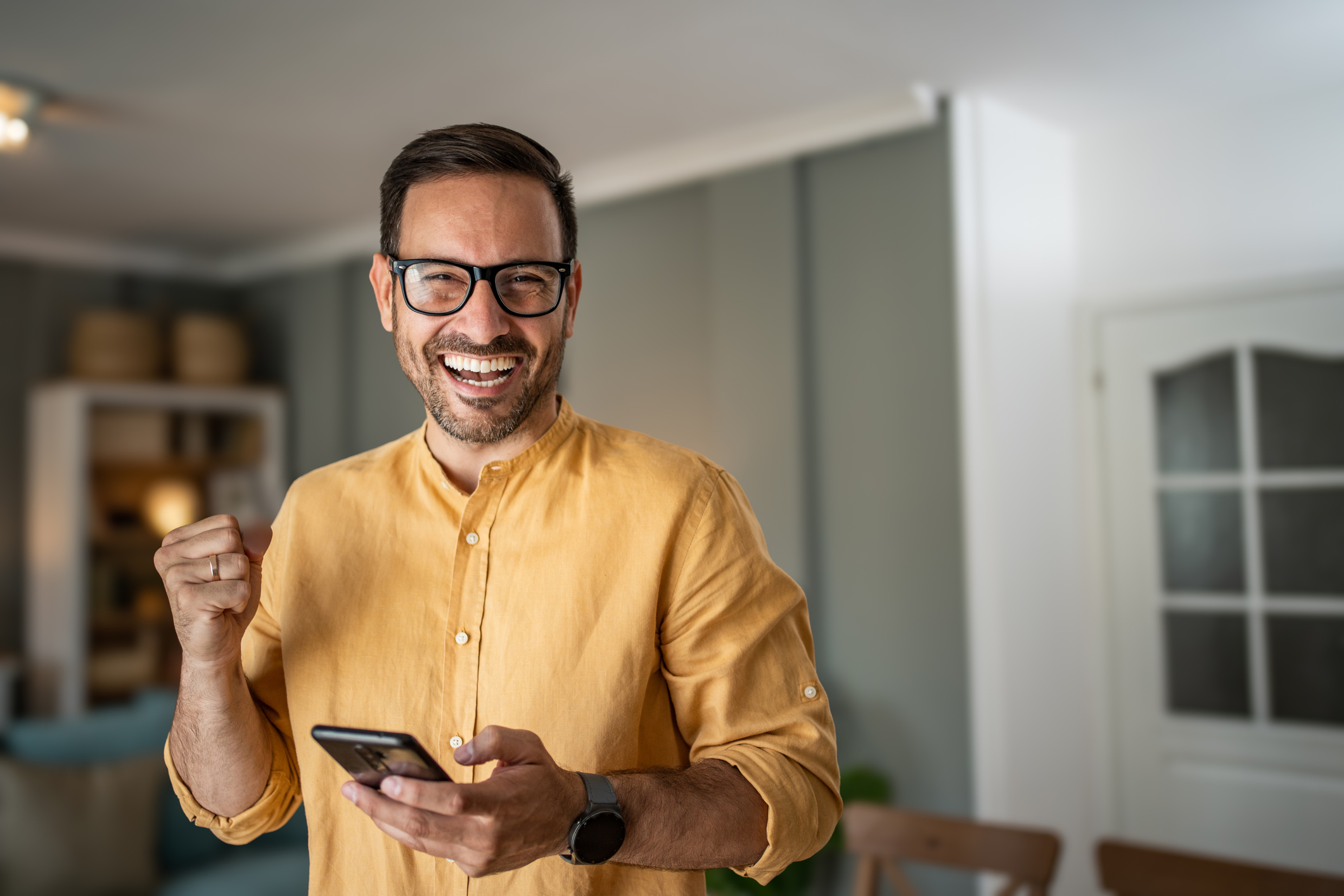 Man happily using smartphone at home in bright living room