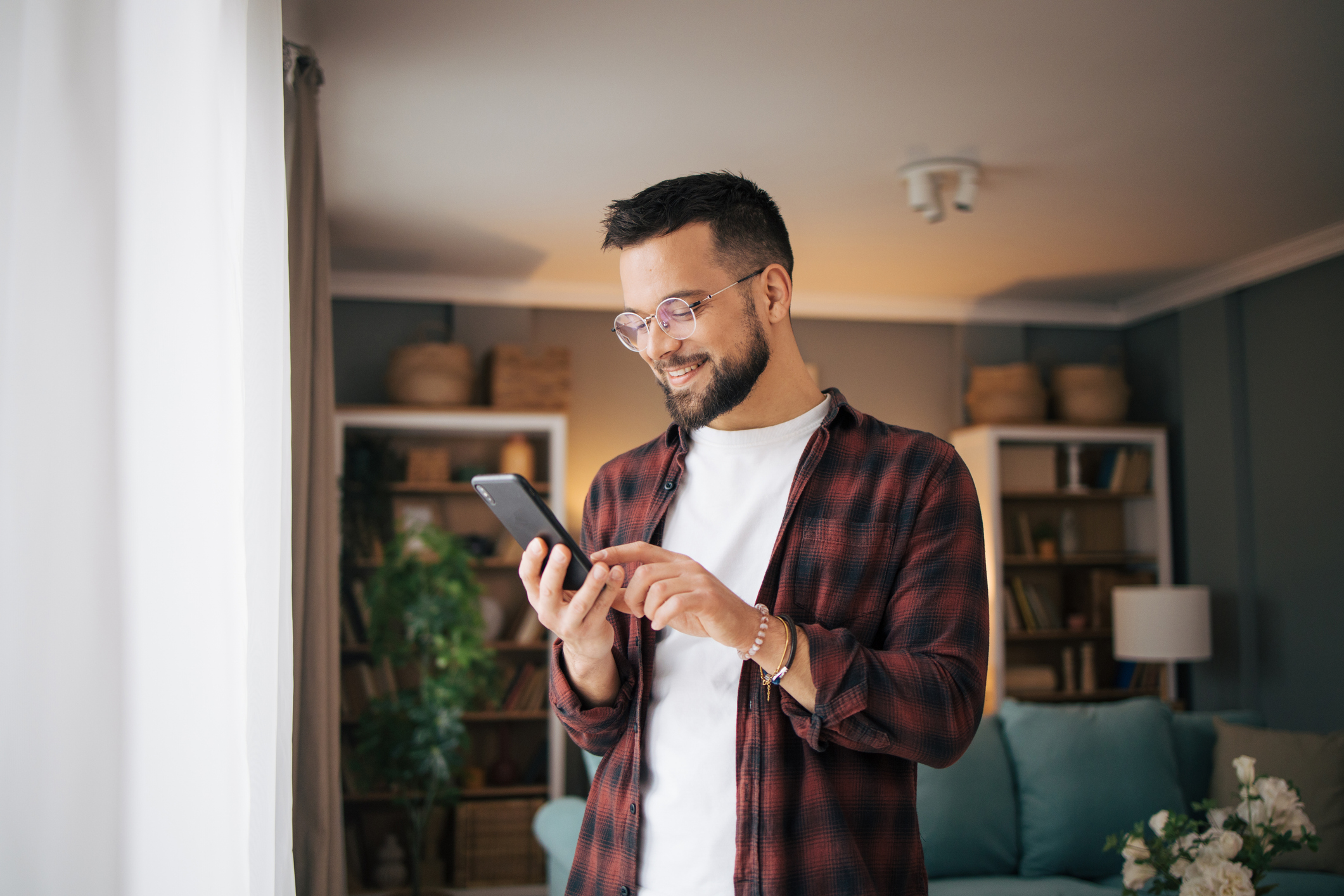 Man smiling while using a smartphone in a cozy living room