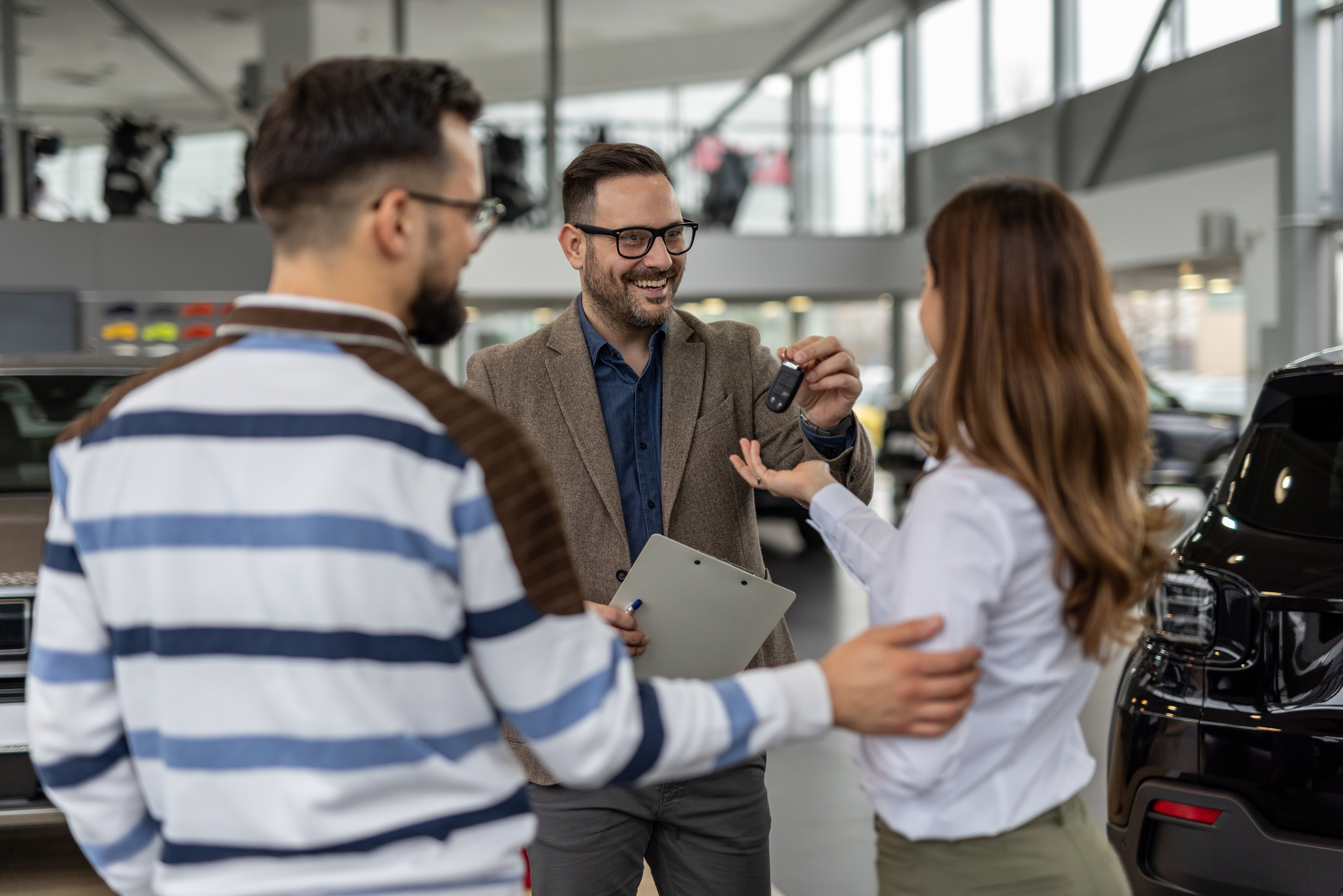 Car dealership staff handing over keys to happy customers