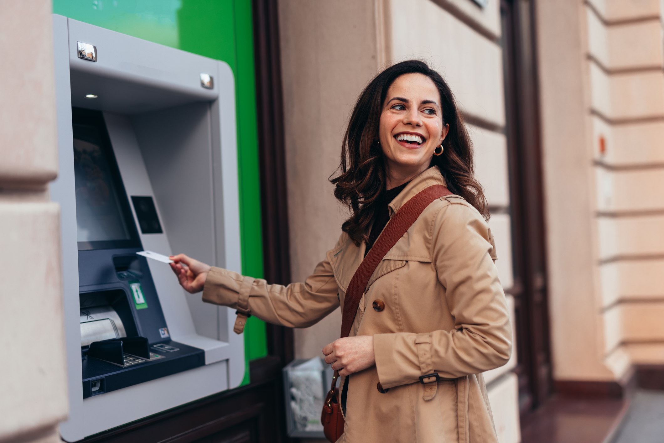 Smiling woman using ATM machine outdoors for cash withdrawal